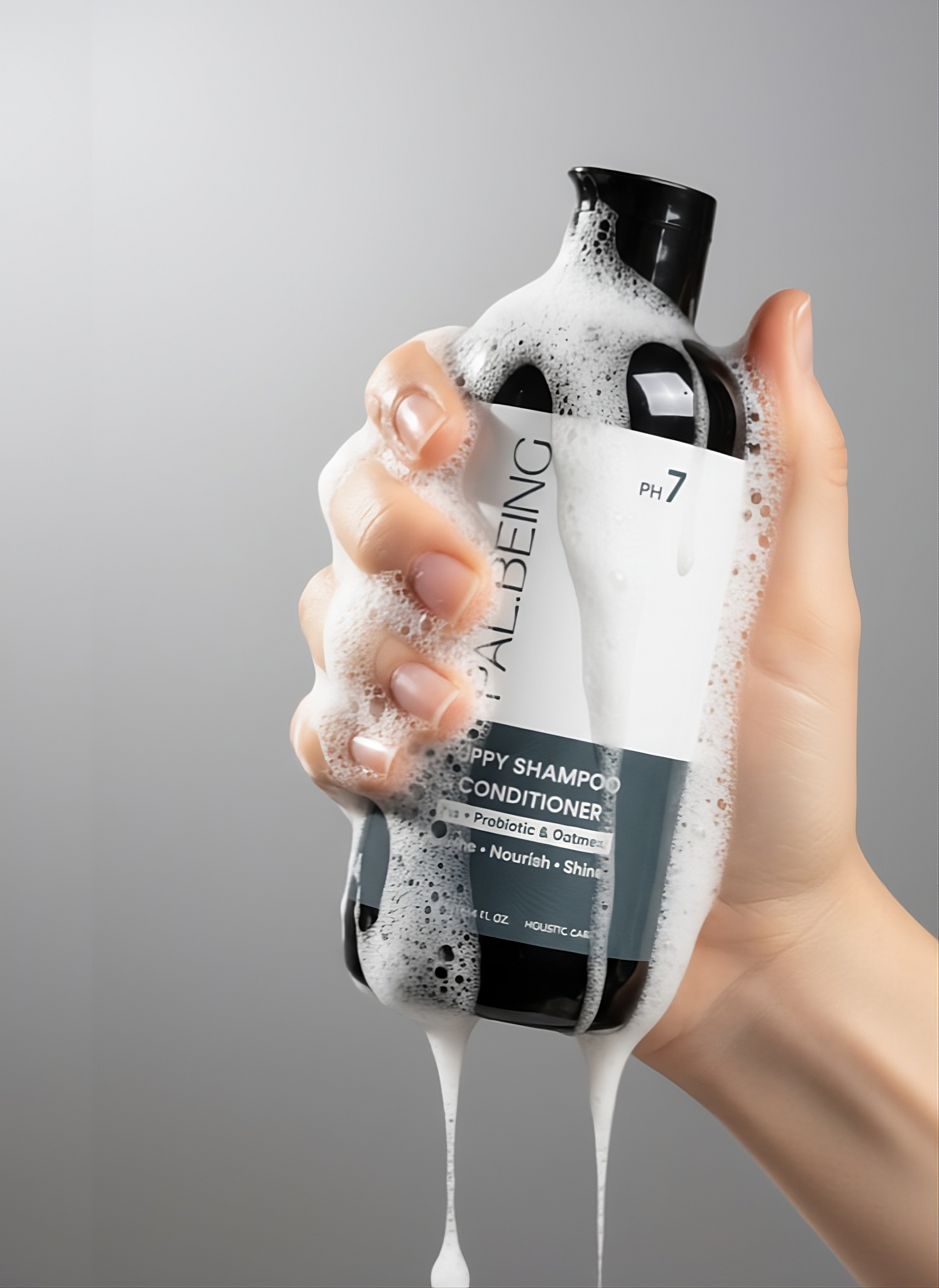 Hand holding a bottle of RealBeing Shampoo &amp; Conditioner with soap suds on a gray background